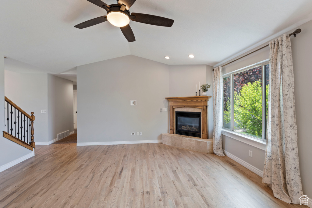 Unfurnished living room with a glass covered fireplace, stairway, wood finished floors, baseboards, and a ceiling fan