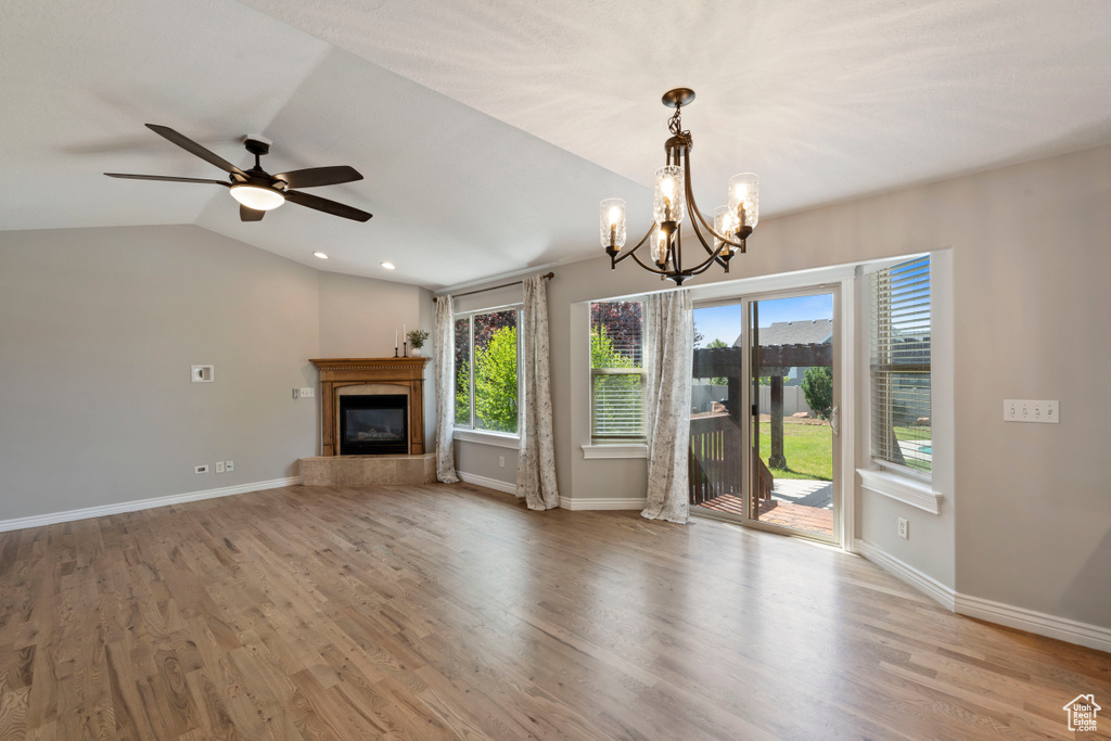 Unfurnished living room with a glass covered fireplace, ceiling fan, baseboards, a chandelier, and lofted ceiling