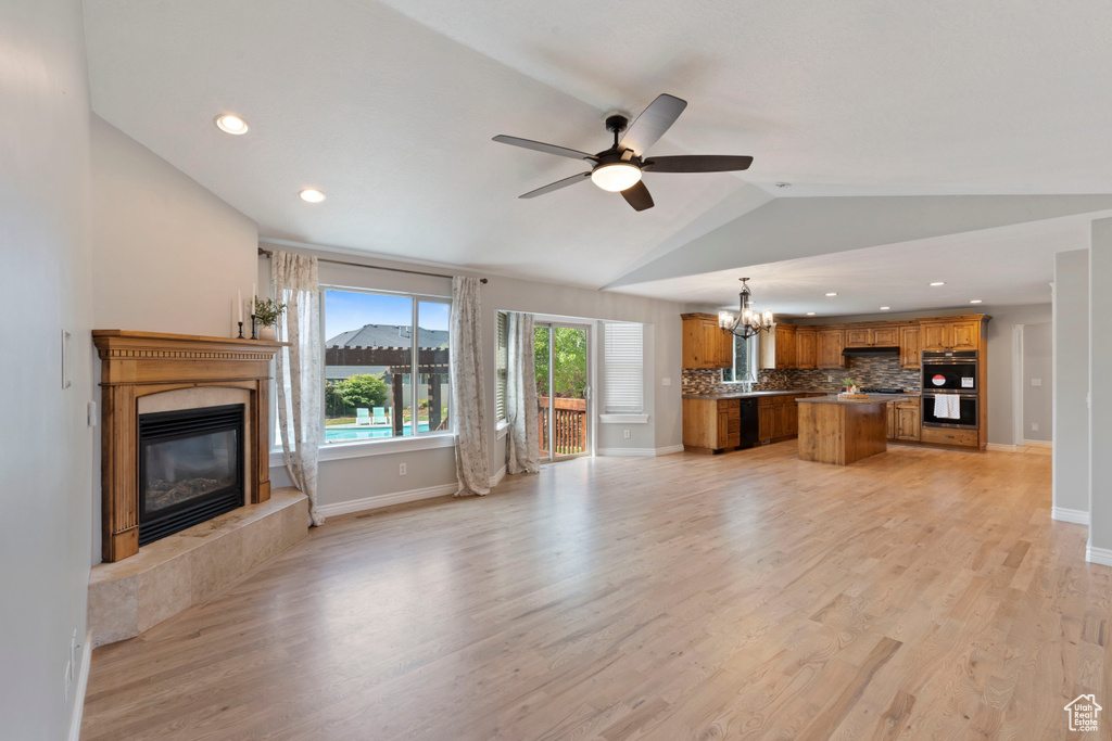Unfurnished living room with a fireplace, a chandelier, vaulted ceiling, a ceiling fan, and light wood-style floors