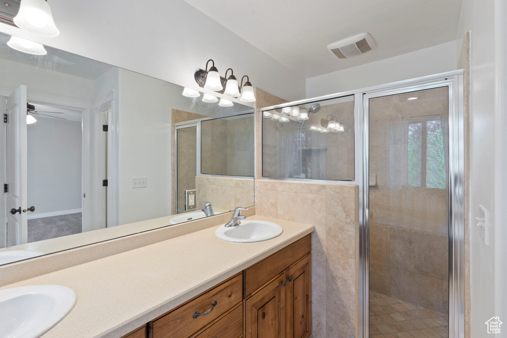 Bathroom with double vanity, a shower stall, ceiling fan, and tile walls