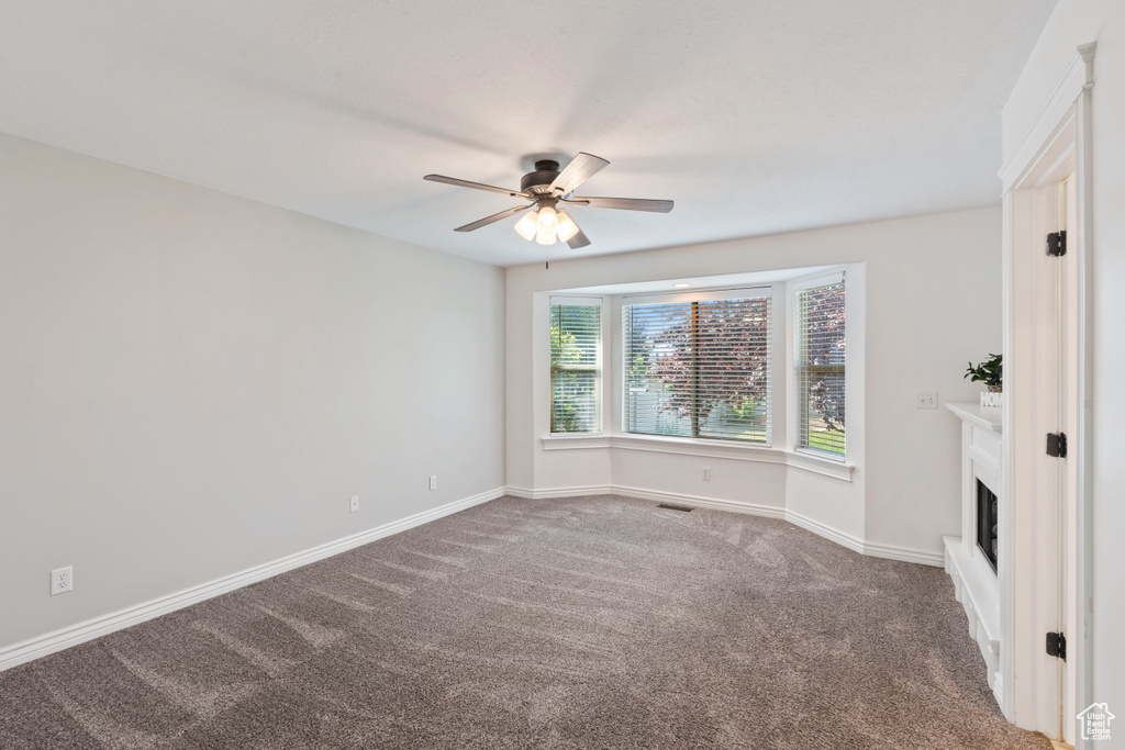 Unfurnished room with ceiling fan, carpet, baseboards, and a fireplace
