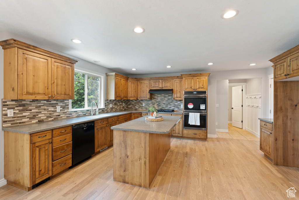 Kitchen featuring black dishwasher, stainless steel double oven, a sink, backsplash, and light wood finished floors
