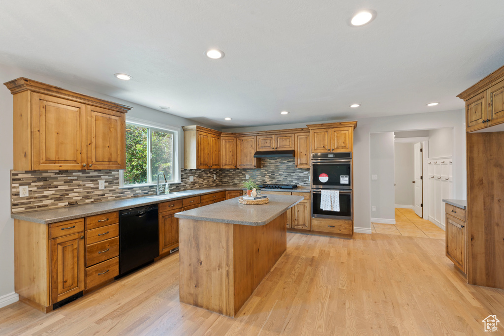 Kitchen with black dishwasher, stainless steel double oven, a sink, tasteful backsplash, and under cabinet range hood