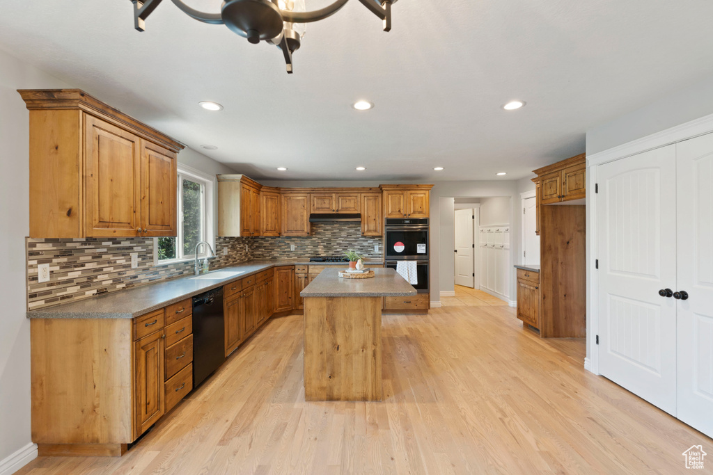 Kitchen with stainless steel appliances, a sink, a center island, backsplash, and light wood-type flooring