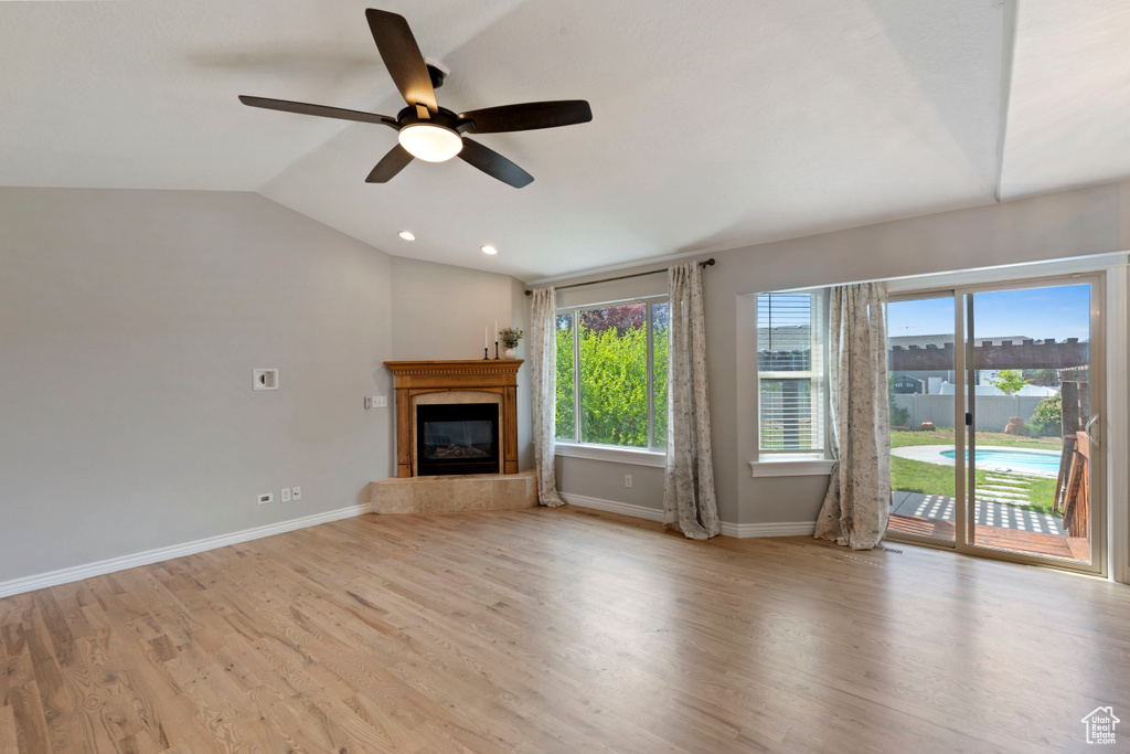 Unfurnished living room with baseboards, a ceiling fan, a glass covered fireplace, vaulted ceiling, and wood finished floors