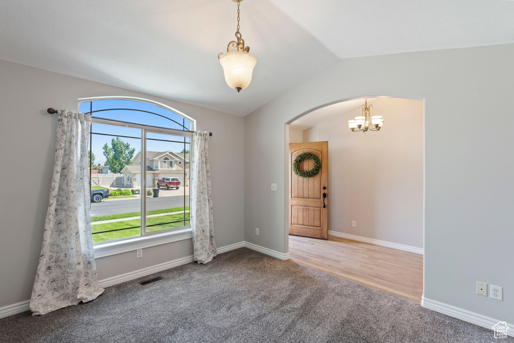 Spare room with arched walkways, a chandelier, plenty of natural light, carpet, and lofted ceiling