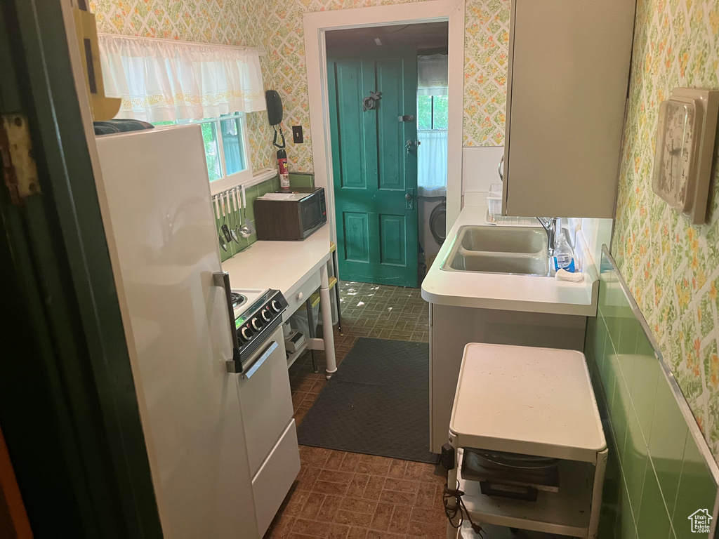 Kitchen with wallpapered walls, white range oven, light countertops, black microwave, and a sink