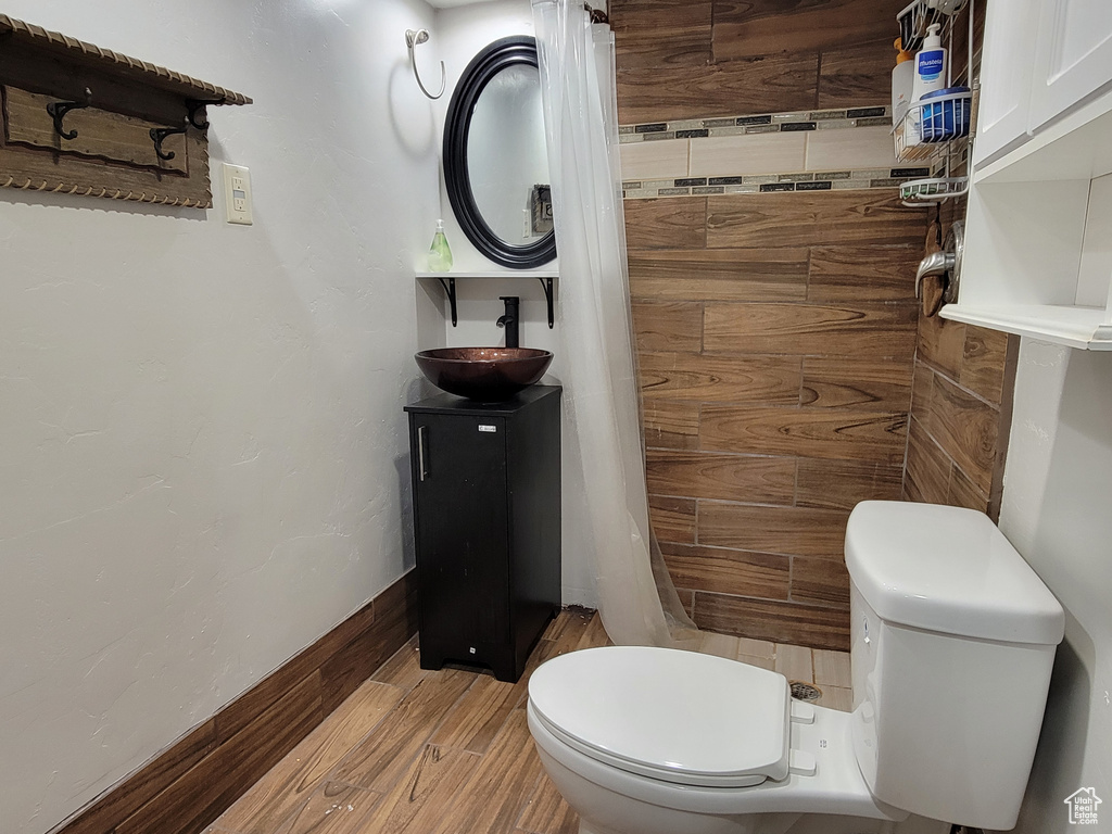 Full bathroom featuring toilet, vanity, tiled shower, and wood finished floors