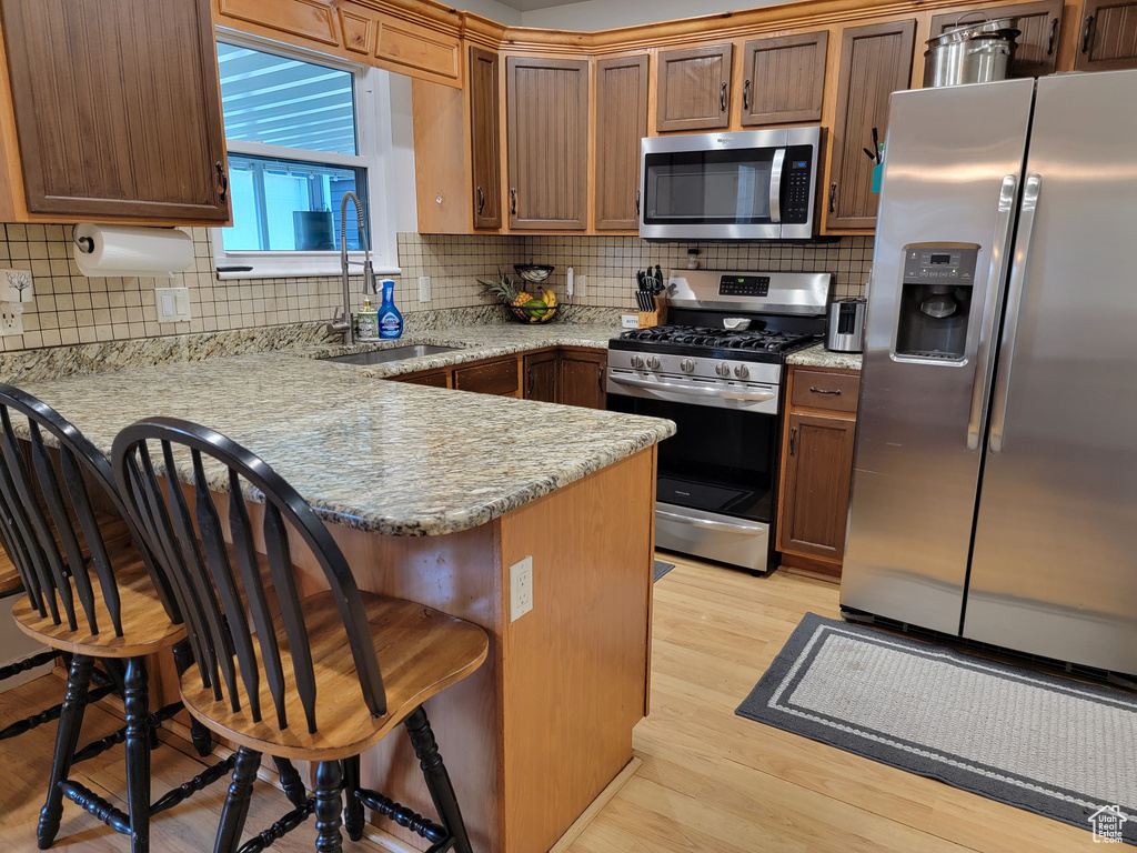 Kitchen with appliances with stainless steel finishes, a sink, a peninsula, a kitchen bar, and light wood finished floors