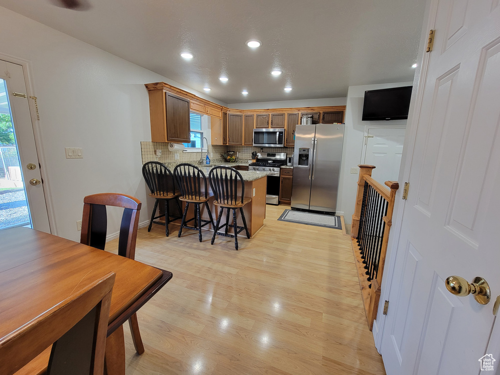 Kitchen featuring stainless steel appliances, a peninsula, tasteful backsplash, light wood-style floors, and a kitchen breakfast bar