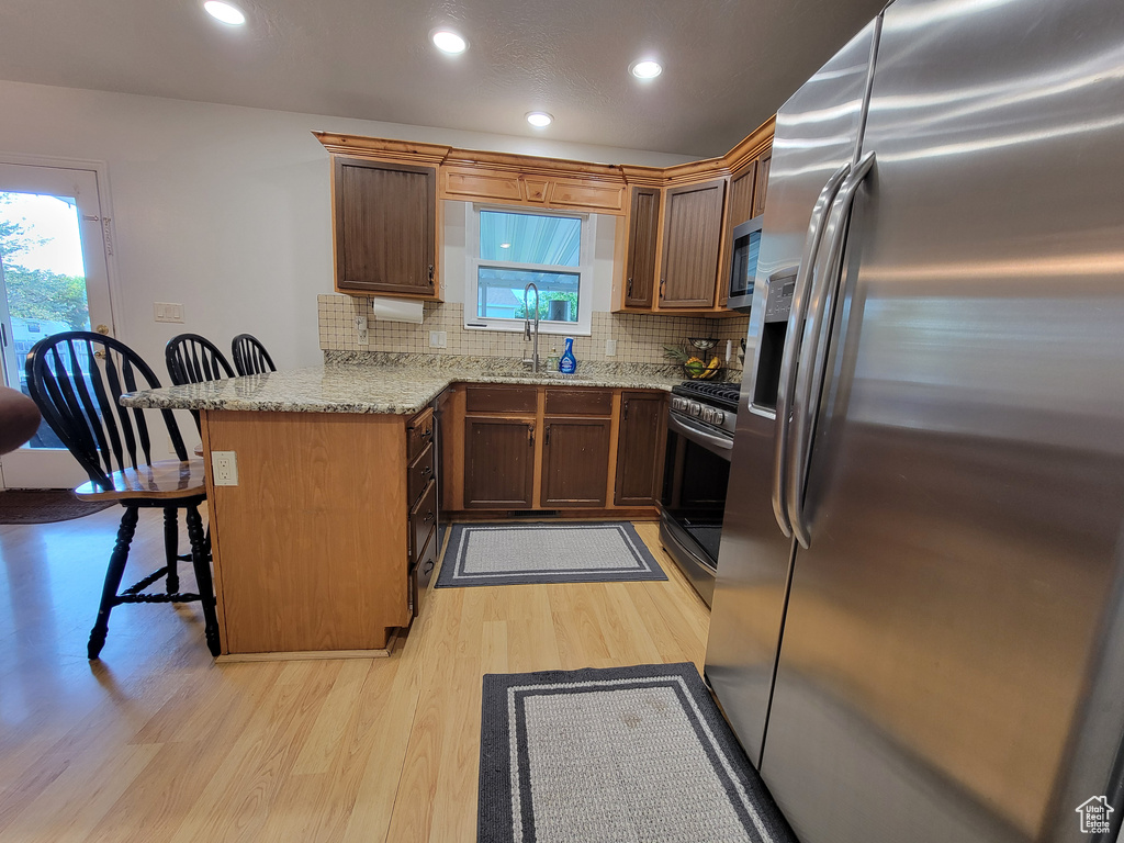 Kitchen featuring appliances with stainless steel finishes, a peninsula, light wood-style flooring, a kitchen bar, and a sink