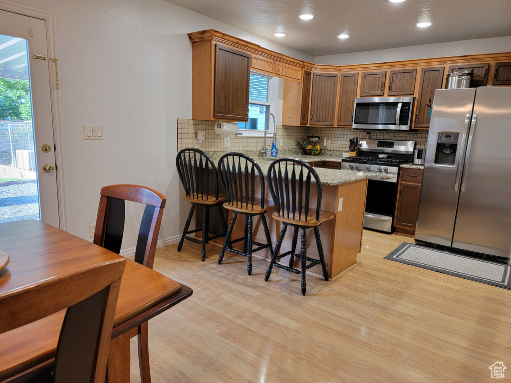 Kitchen with stainless steel appliances, a peninsula, light wood-type flooring, decorative backsplash, and recessed lighting