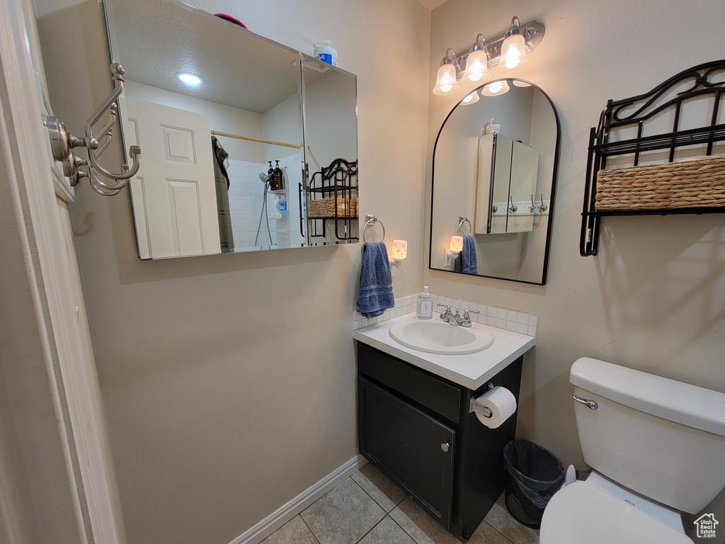 Bathroom featuring tile patterned flooring, vanity, toilet, baseboards, and a shower