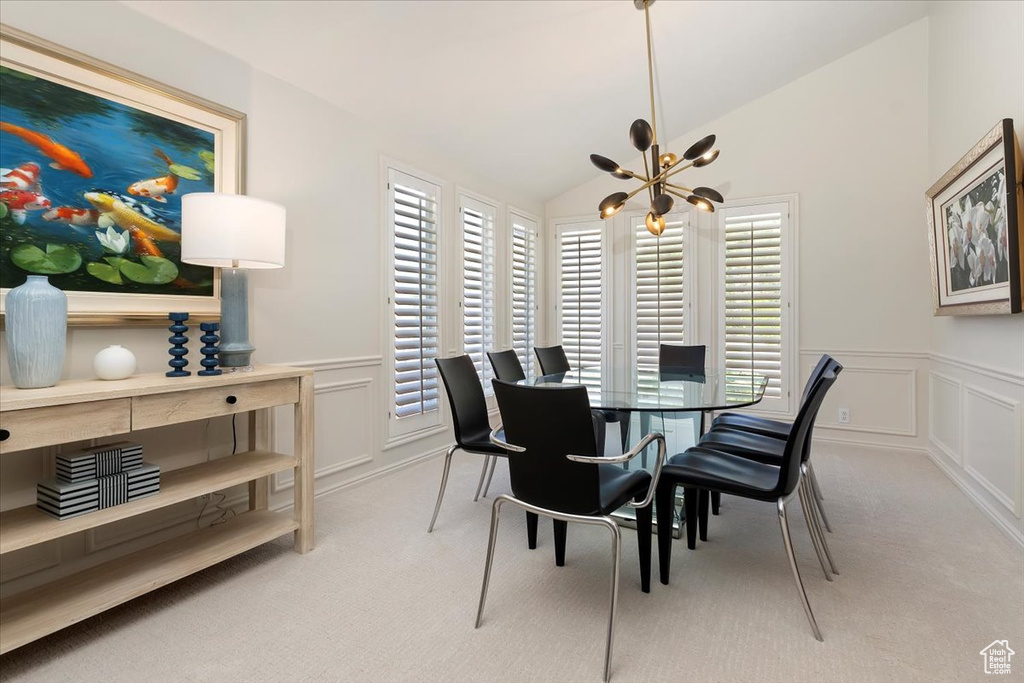 Carpeted dining area featuring a chandelier, a decorative wall, healthy amount of natural light, lofted ceiling, and a wainscoted wall