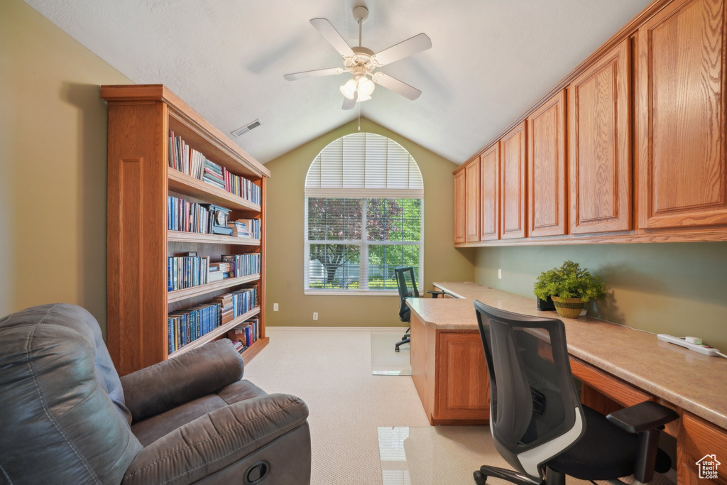 Office space with built in desk, vaulted ceiling, ceiling fan, light colored carpet, and baseboards