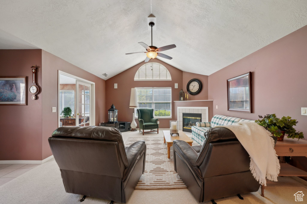 Living area featuring ceiling fan, a textured ceiling, a tiled fireplace, vaulted ceiling, and light carpet