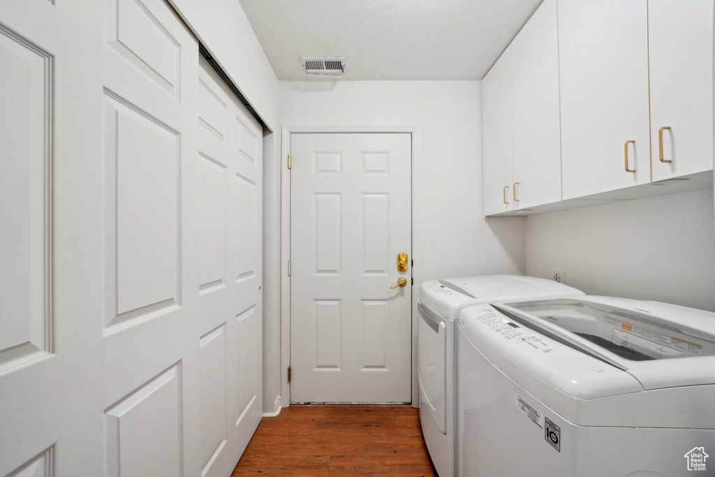 Washroom featuring cabinet space, washing machine and clothes dryer, and light wood-type flooring