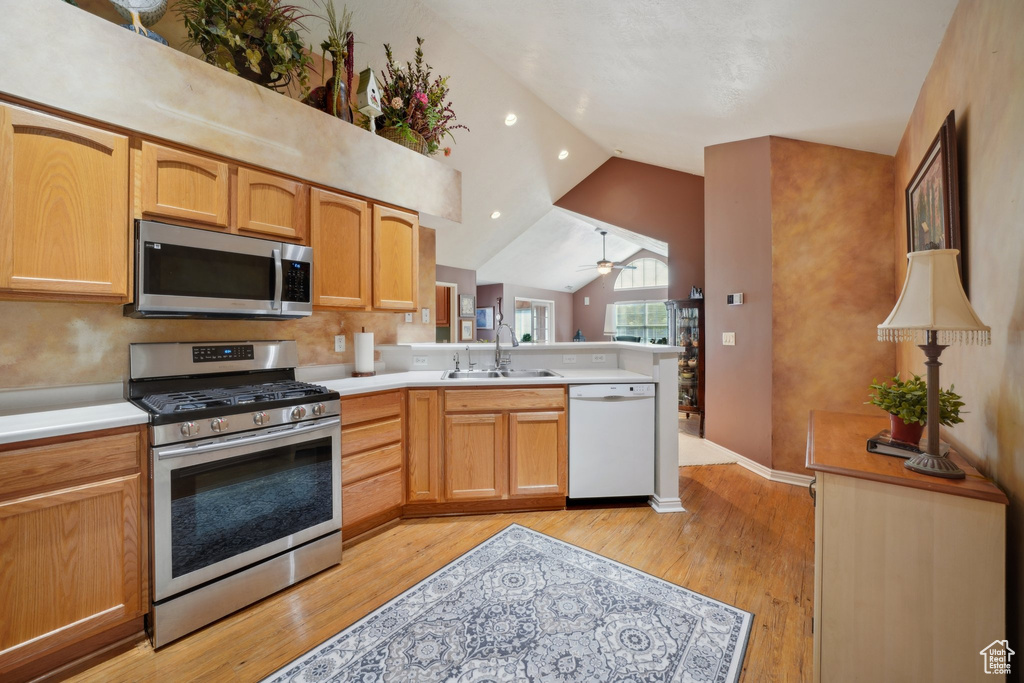 Kitchen featuring appliances with stainless steel finishes, a sink, vaulted ceiling, a peninsula, and light wood-type flooring