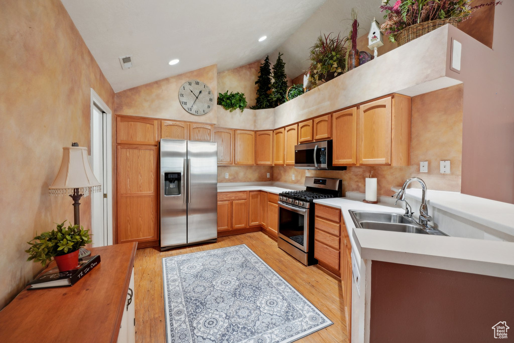 Kitchen featuring appliances with stainless steel finishes, a sink, light countertops, light wood finished floors, and high vaulted ceiling
