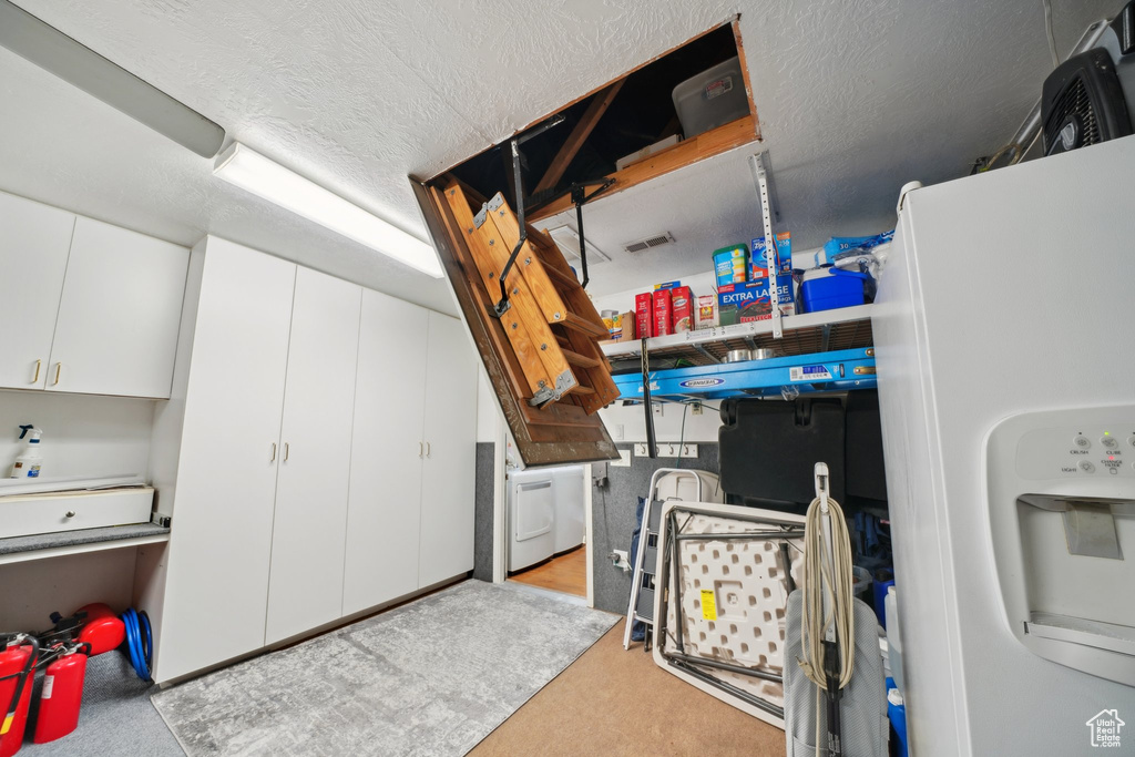 Garage with white refrigerator with ice dispenser and washer / clothes dryer