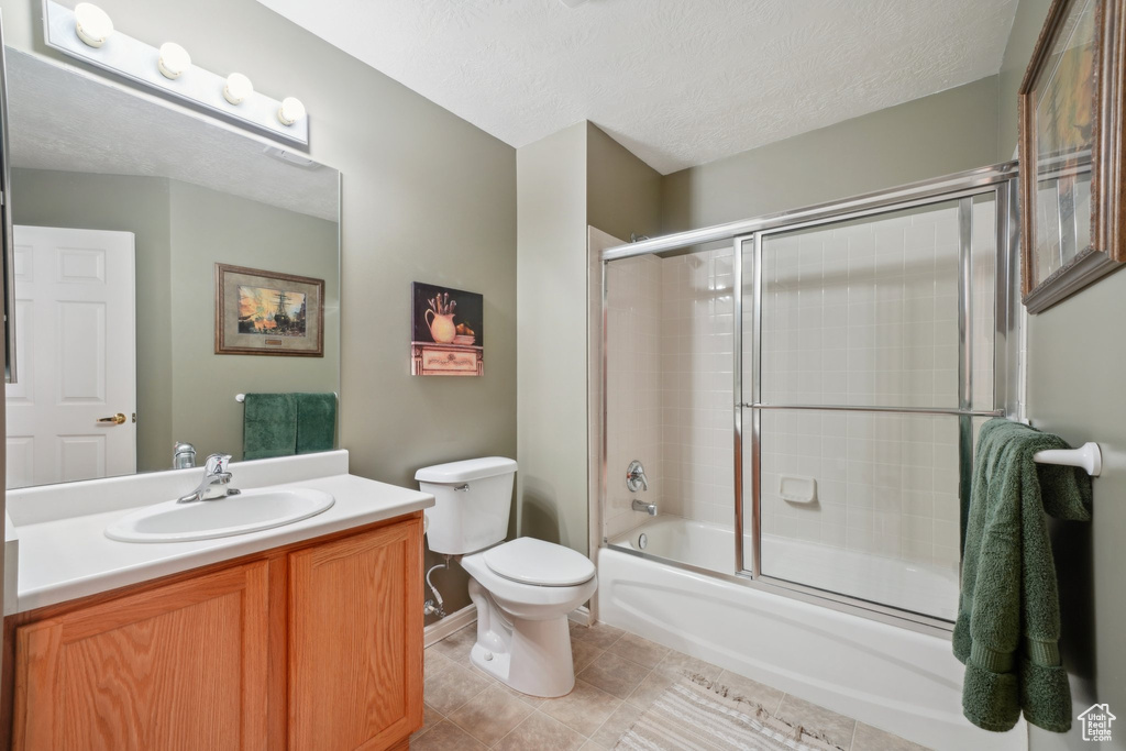 Bathroom with toilet, vanity, combined bath / shower with glass door, tile patterned flooring, and a textured ceiling