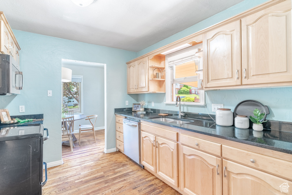 Kitchen with dishwashing machine, a sink, light brown cabinets, range, and stainless steel microwave