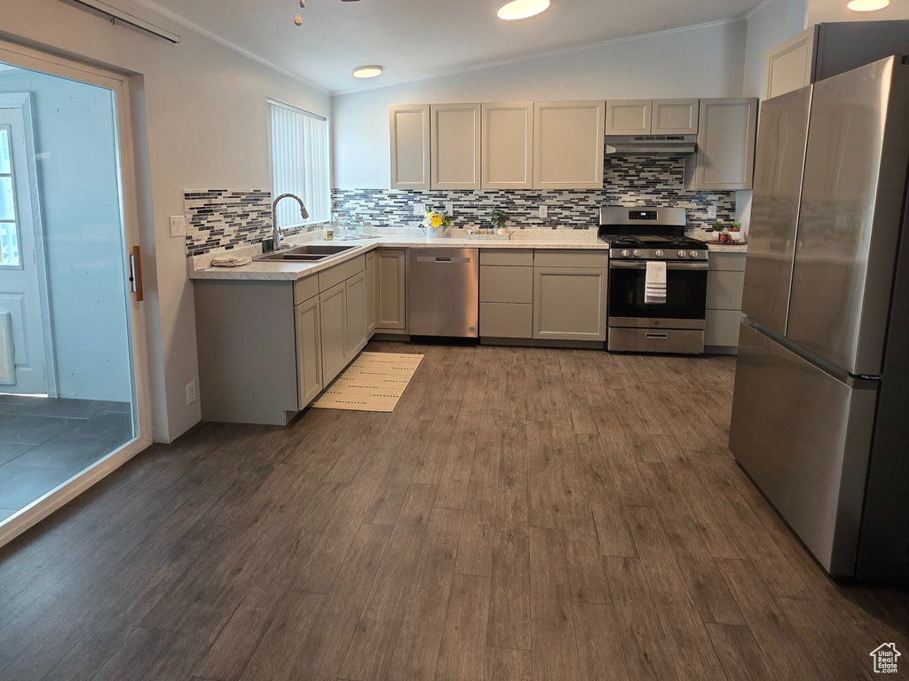 Kitchen with appliances with stainless steel finishes, a sink, light countertops, and backsplash
