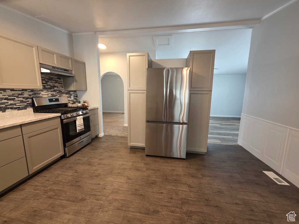 Kitchen with stainless steel appliances, under cabinet range hood, arched walkways, tasteful backsplash, and gray cabinets