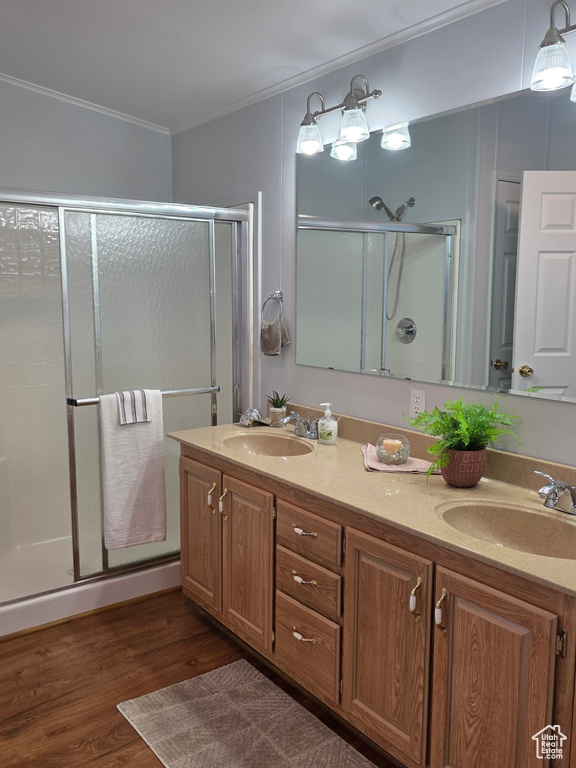 Bathroom with ornamental molding, a stall shower, double vanity, and wood finished floors