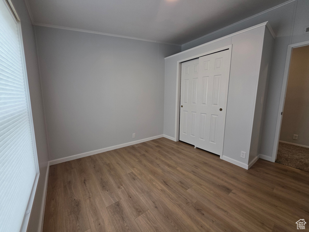Unfurnished bedroom featuring ornamental molding, wood finished floors, baseboards, a closet, and multiple windows