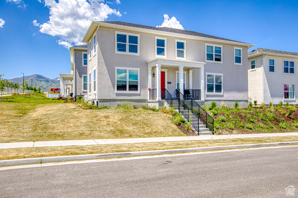 View of front of home featuring a mountain view, a porch, stucco siding, and a front lawn