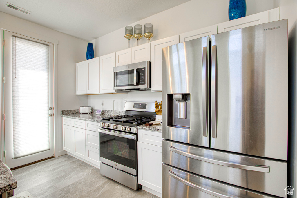Kitchen featuring appliances with stainless steel finishes, light stone countertops, and white cabinetry
