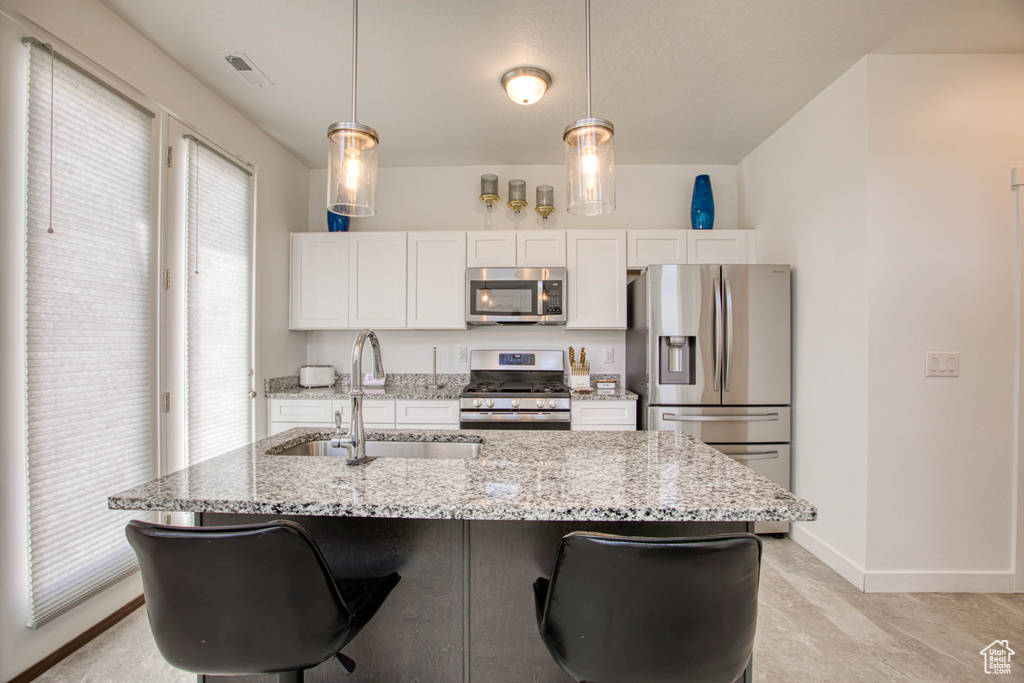 Kitchen featuring appliances with stainless steel finishes, a sink, white cabinetry, a center island with sink, and baseboards