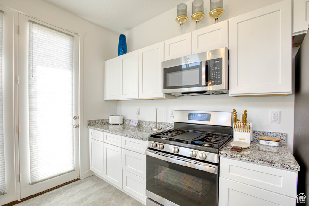 Kitchen with appliances with stainless steel finishes, white cabinetry, and light stone counters