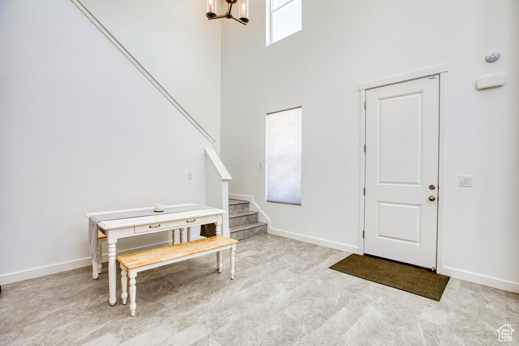 Foyer featuring stairs, a towering ceiling, a chandelier, and baseboards