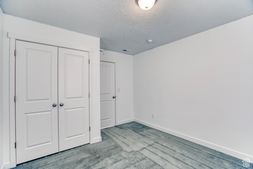 Unfurnished bedroom with carpet, a closet, a textured ceiling, and baseboards