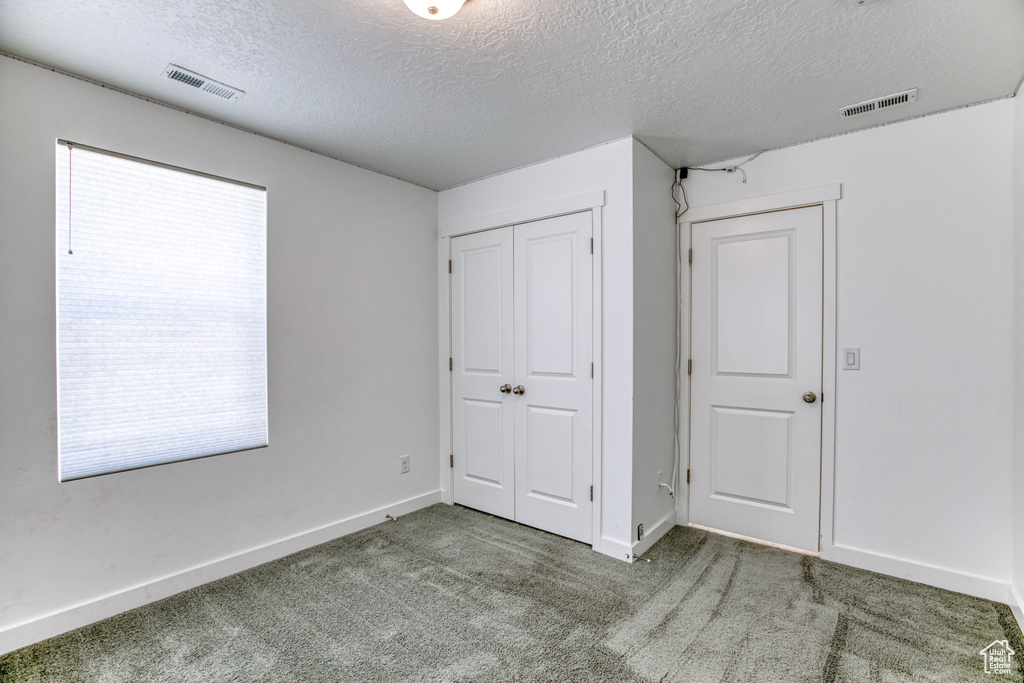 Unfurnished bedroom with a textured ceiling, carpet, baseboards, and a closet