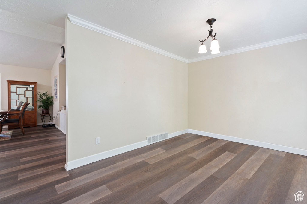 Empty room with a chandelier, dark wood finished floors, baseboards, and crown molding