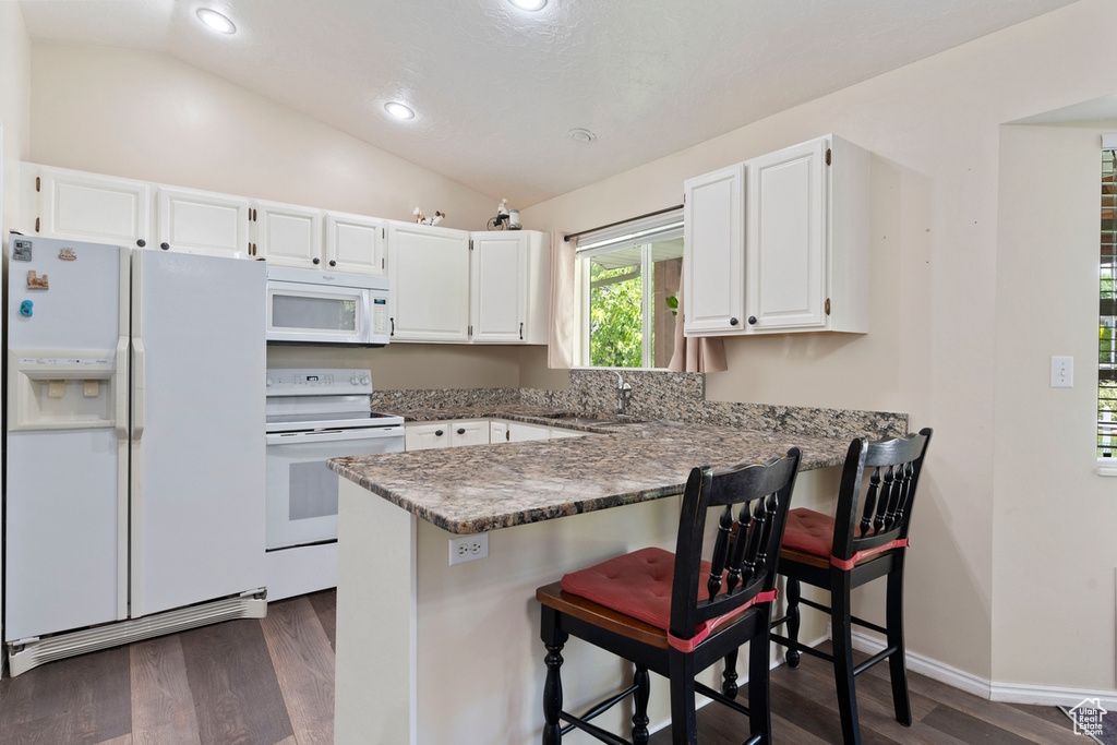 Kitchen featuring white appliances, dark wood finished floors, vaulted ceiling, a peninsula, and white cabinetry
