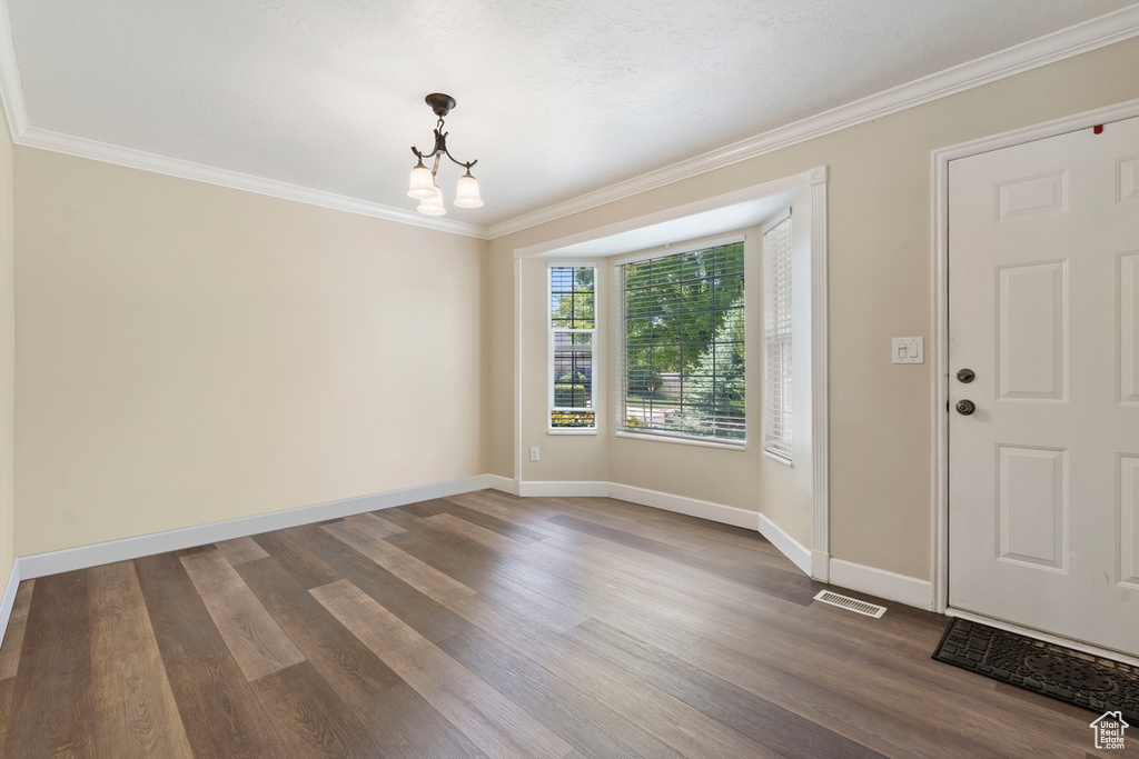 Foyer entrance with a chandelier, crown molding, dark wood-style flooring, and baseboards