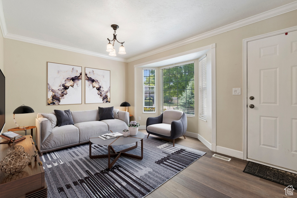 Living area with ornamental molding, wood finished floors, baseboards, and a chandelier