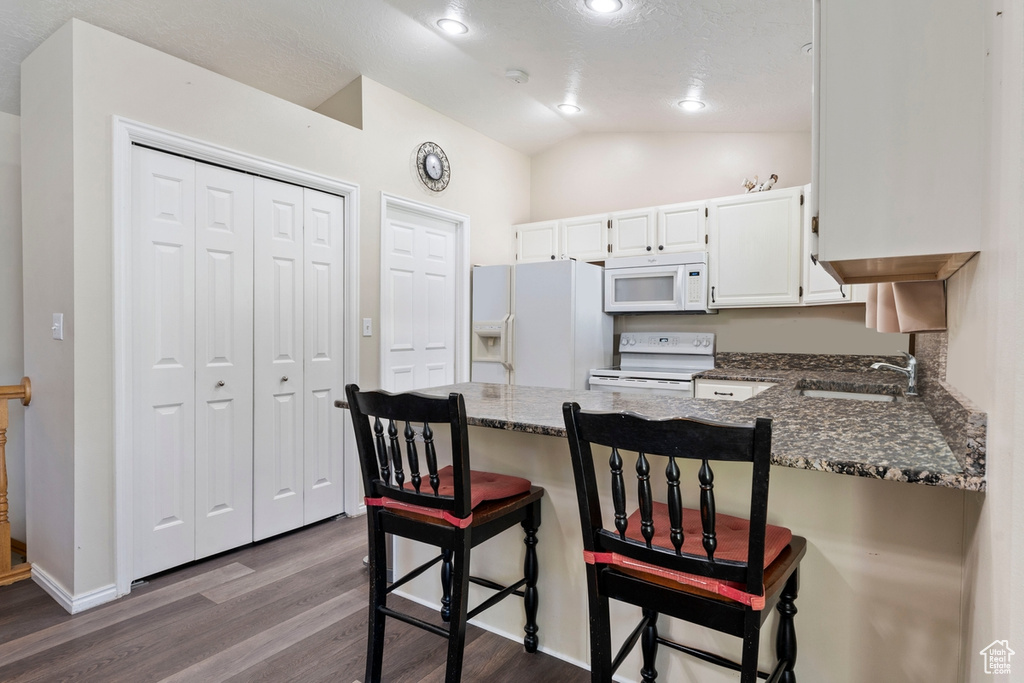 Kitchen featuring white appliances, dark wood finished floors, a sink, a peninsula, and dark stone counters