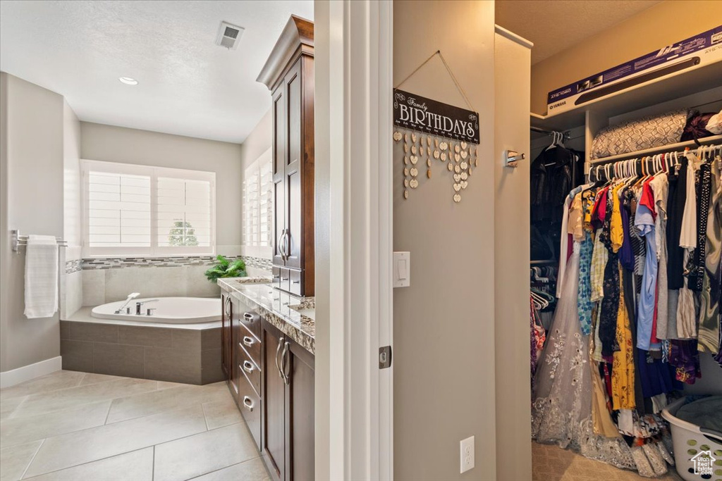 Bathroom with vanity, a garden tub, a walk in closet, tile patterned floors, and baseboards