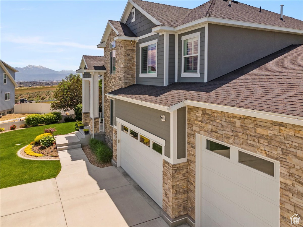 View of property exterior with stone siding, a shingled roof, an attached garage, a yard, and a mountain view
