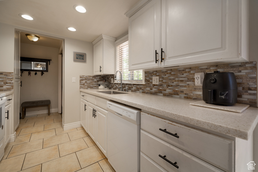Kitchen featuring white dishwasher, a sink, light tile patterned floors, tasteful backsplash, and white cabinetry