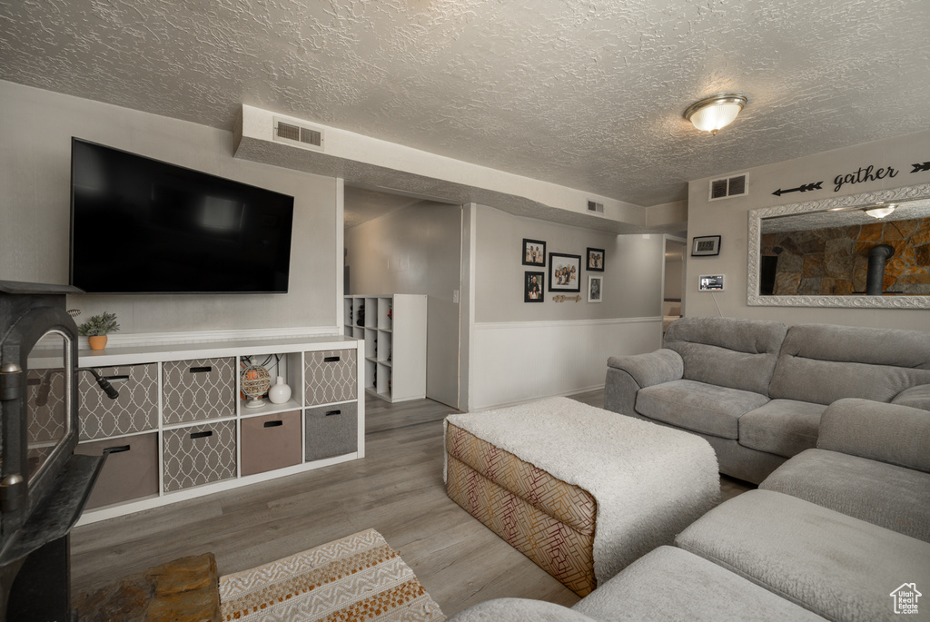 Living room with a textured ceiling, a wood stove, and wood finished floors