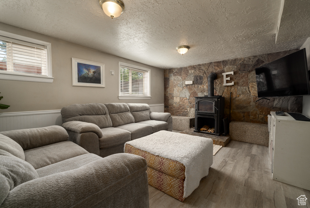 Living room featuring a textured ceiling, a wood stove, light wood finished floors, and a wainscoted wall
