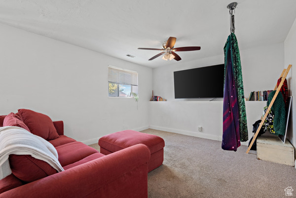 Carpeted living area featuring ceiling fan and baseboards