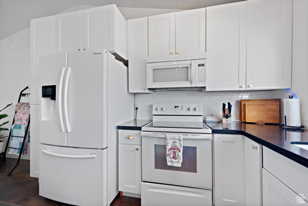 Kitchen with white appliances, dark countertops, white cabinetry, and tasteful backsplash