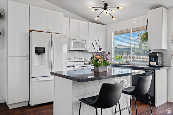Kitchen with white appliances, a sink, tasteful backsplash, dark countertops, and lofted ceiling
